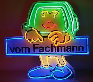 Neonschild mit einer Comicfigur, die ein blaues Schild mit der Aufschrift „vom Fachmann“ in Gelb, Grün und Blau hält.