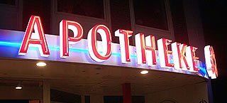 Apothekenschild leuchtet in rotem Neon vor dunklem Hintergrund.