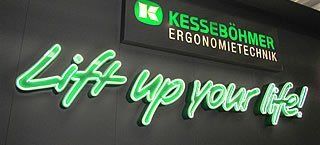 Schild mit neongrüner Aufschrift „Lift up your life!“ unter dem Firmennamen „KESSEBÖHMER ERGONOMIE TECHNIK“.