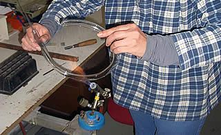 Person, die mit einem Brenner Glasröhren formt, wahrscheinlich in einer Werkstatt.