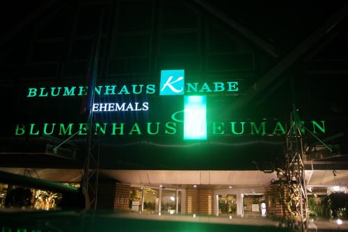 Grünes Leuchtschild: Blumenhaus Knabe ehemals Blumenhaus Neumann über einem Gebäudeeingang bei Nacht.