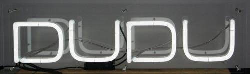 Neonschild mit der Aufschrift „DUDU“ in Weiß auf grauem Hintergrund.