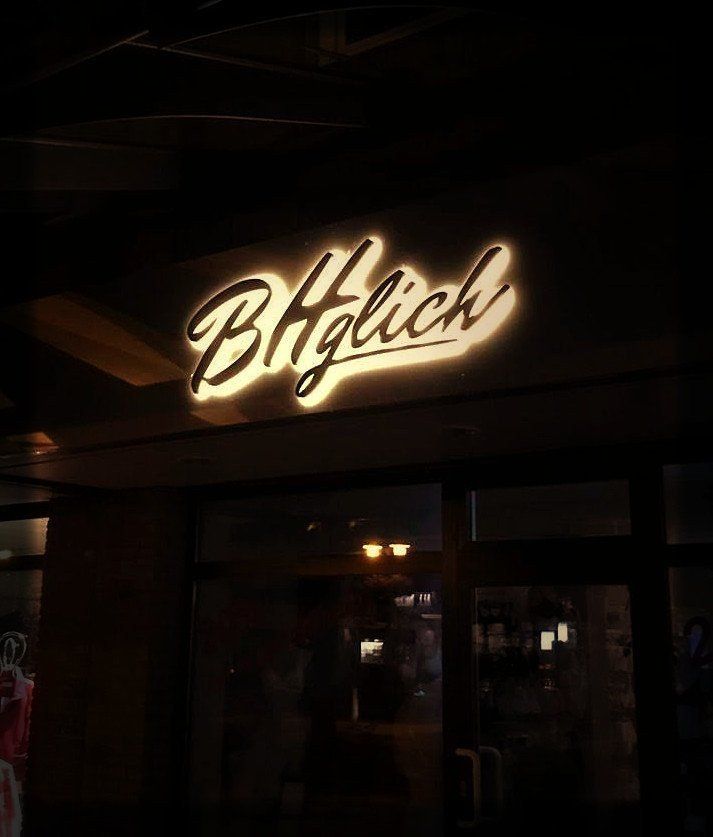 Beleuchtetes „B. Häglich“-Schild über einem dunklen Eingang.