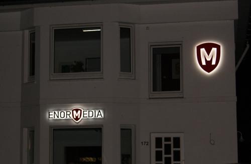 Beleuchtetes ENOR MEDIA-Schild und -Schildlogo auf der weißen Außenseite eines Gebäudes bei Nacht.