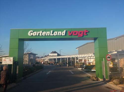Grüner Eingangstorbogen zum Gartencenter GartenLand Vogt, im Hintergrund Gebäude, blauer Himmel.