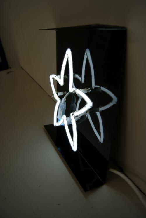 Neonlichtskulptur eines weißen Atomsymbols vor einem dunkelschwarzen Hintergrund.