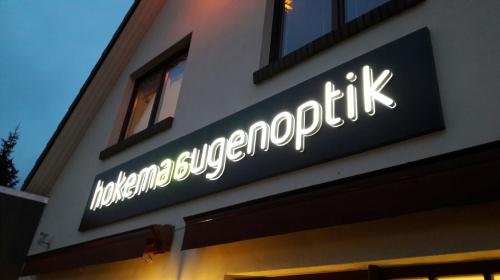 Schild für „hakema augenoptik“ in weißer Schrift auf dunklem Rechteck, angebracht an einer Gebäudefassade.