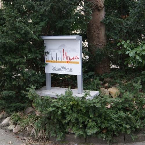 Schild für das Hotel Weimar in einer Gartenanlage mit grünen Büschen.