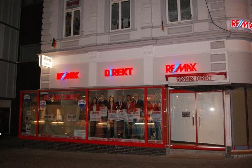 RE/MAX-Immobilienbüro bei Nacht mit leuchtenden roten Schildern und Mitarbeitern im Fenster.