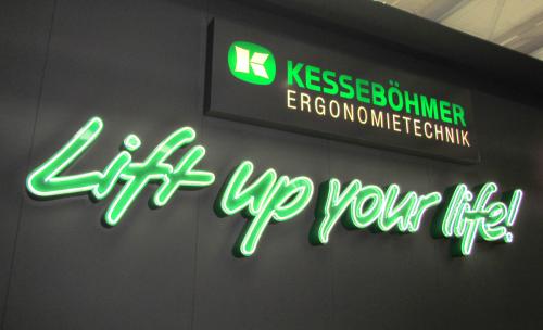 Schild: „Lift up your life!“ in Neongrün, unter Kesseböhmer-Logo und Firmenname. Schwarzer Hintergrund.