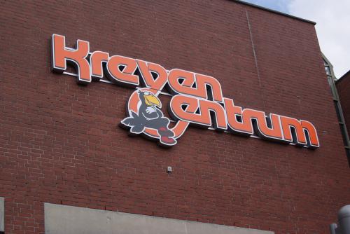 Orangefarbenes „Kreva Centrum“-Schild mit Logo auf einem Backsteingebäude.