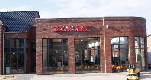 „BUNUES-Laden mit Backsteinfassade, großen Fenstern und einem gelben Gabelstapler davor.“