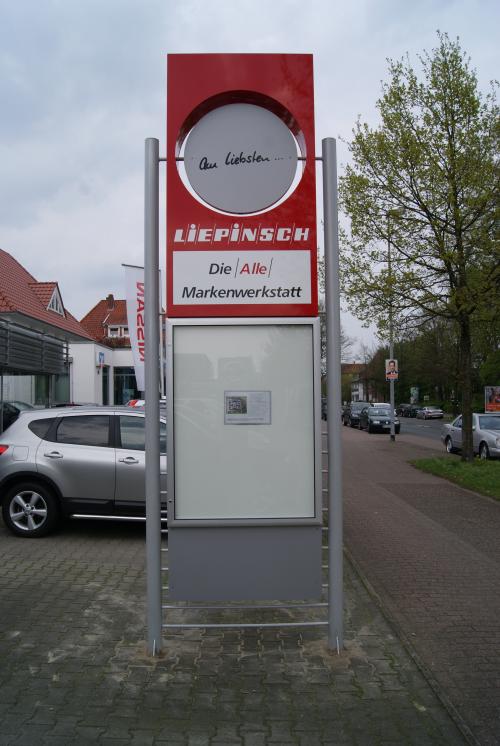Schild „LIEPINSCH“ Autowerkstatt, rot und silber, auf einem gepflasterten Gehweg.