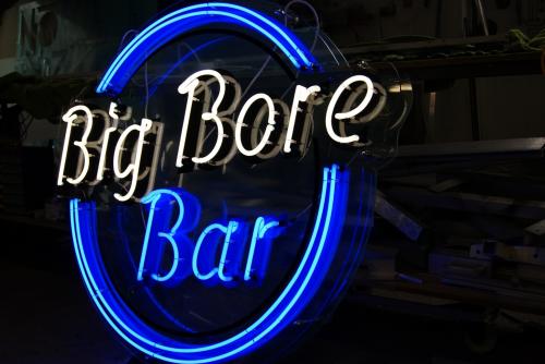 Neonschild für „Big Bore Bar“ mit weißen und blauen Lichtern in dunkler Umgebung.