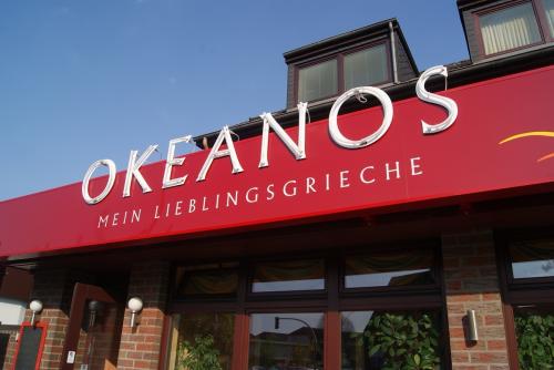Schild für das Restaurant Okeanos, roter Hintergrund mit weißen Buchstaben, „OKEANOS“ und „Mein Lieblingsgrieche“.