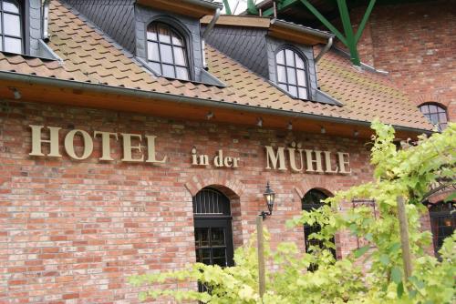 Hotelschild „in der Mühle“ auf Backsteingebäude mit Ziegeldach, Weinreben im Vordergrund.