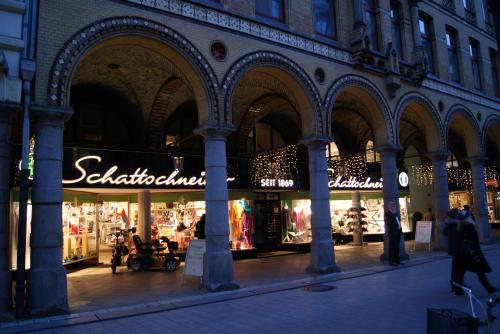 Gebäudefassade mit gewölbtem Gang, Schaufenstern und Menschen. „Schattschneider“-Schild sichtbar.