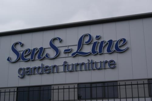 „Schild des Gartenmöbelgeschäfts SenS-Line, blaue Schrift auf weißem Gebäude.“