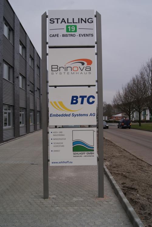 Wegweiser mit Firmenlogos vor einem modernen Gebäude.