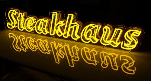 Gelbes Neonschild „Steakhaus“ mit seiner Spiegelung.
