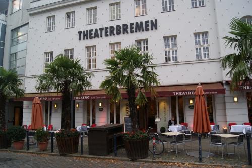 Theatergebäude Bremen mit Außensitzplätzen und Palmen.