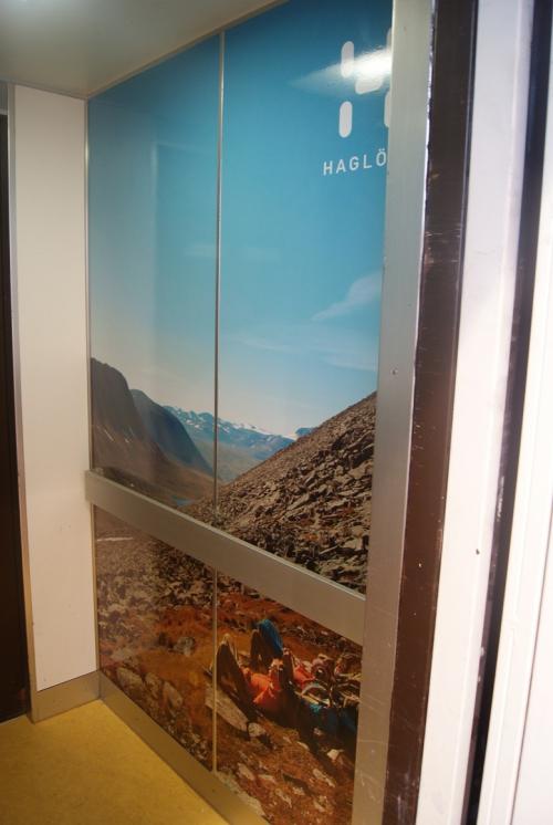 Glastür mit Bergszene und „Haglöfs“-Logo; am Sockel sind zwei Figuren sichtbar.