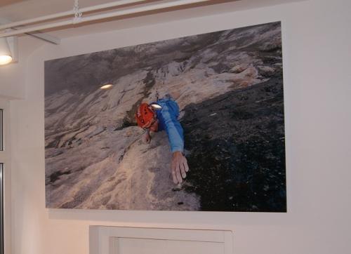 Kletterer an einer Felswand; er greift mit Helm in einer rauen Berglandschaft nach einem Halt.