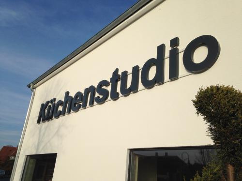 „Küchenstudio“-Schild auf einem weißen Gebäude, im Hintergrund blauer Himmel.