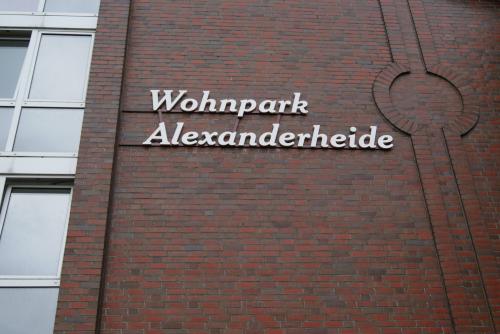 Schild „Wohnpark Alexanderheide“ an einem Backsteingebäude mit Fenstern auf der linken Seite.