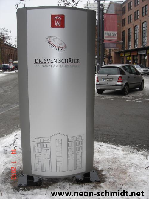 Schild für Zahnarzt „Dr. Sven Schäfer“. Silbernes Schild mit Logo und Gebäudeabbildung auf einer verschneiten Straße.