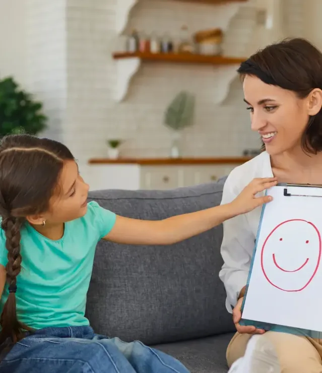 A woman is sitting on a couch holding a clipboard with a smiley face drawn on it.