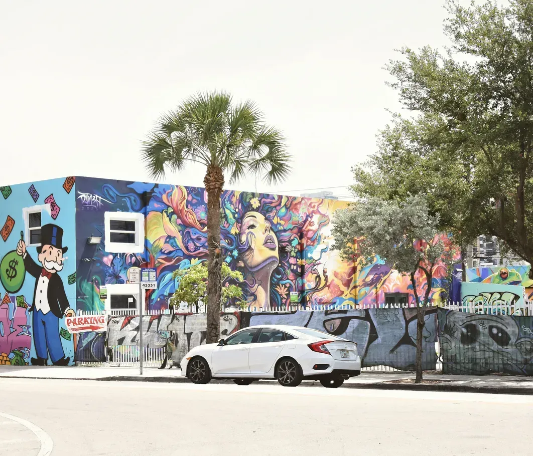 A white car is parked in front of a building with a mural on it.