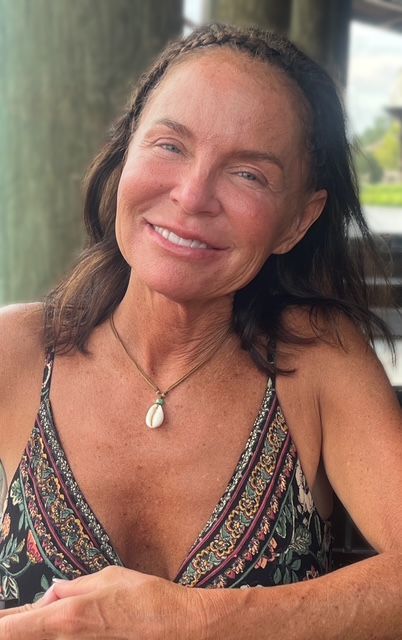 A woman wearing sunglasses and a necklace is smiling for the camera.