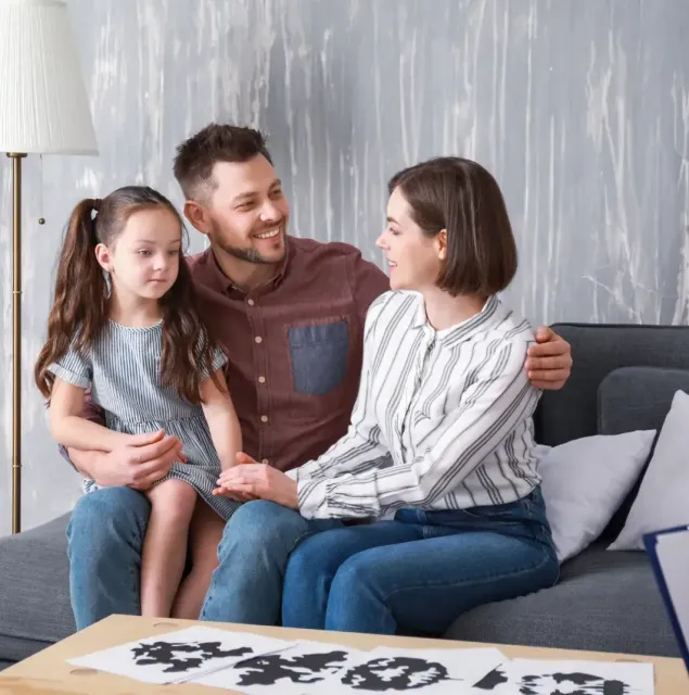 A family is sitting on a couch talking to a woman.