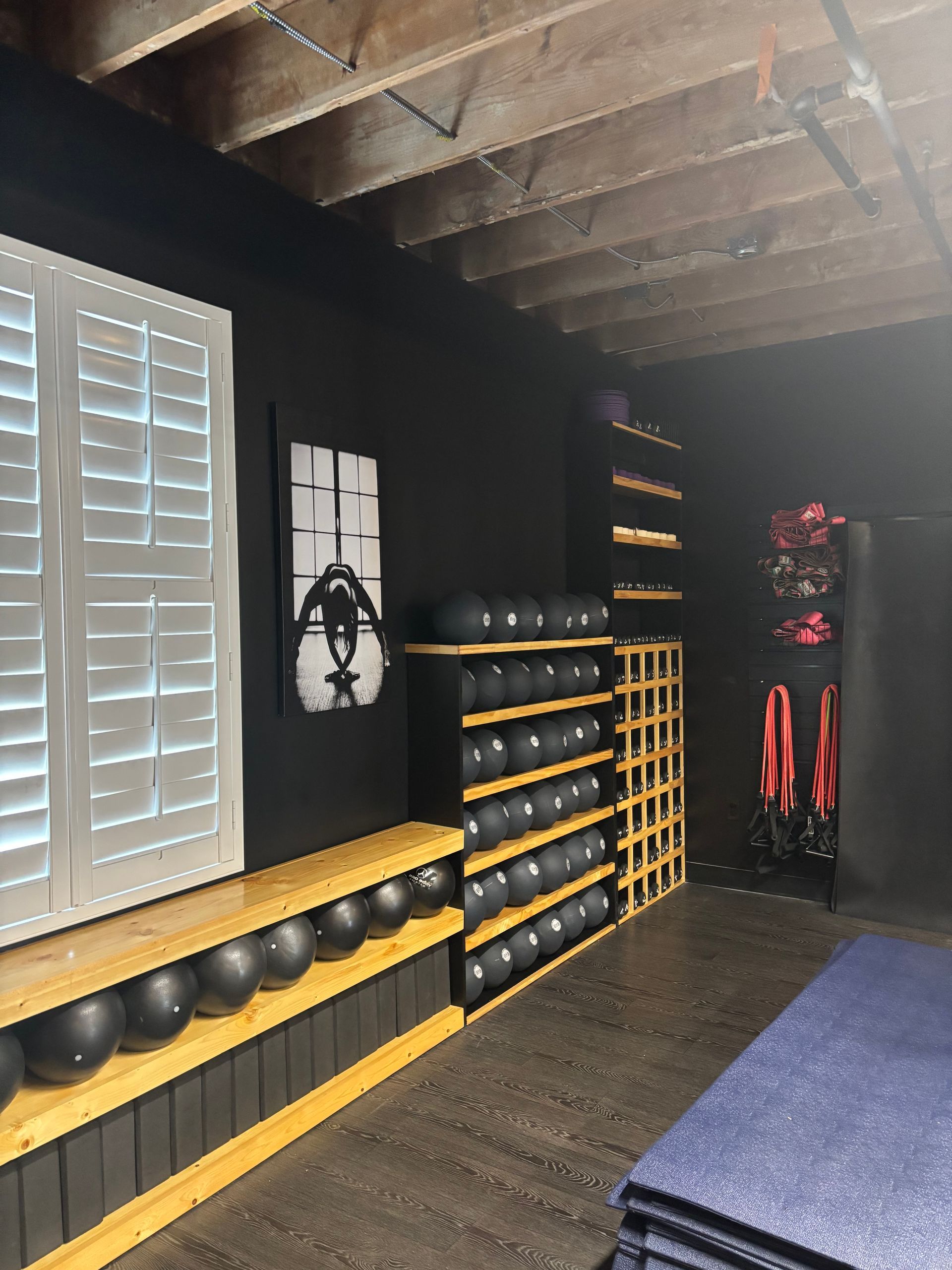 Gym interior with exercise balls, shelving, and exercise equipment. Black walls, wooden shelves, blue mats.