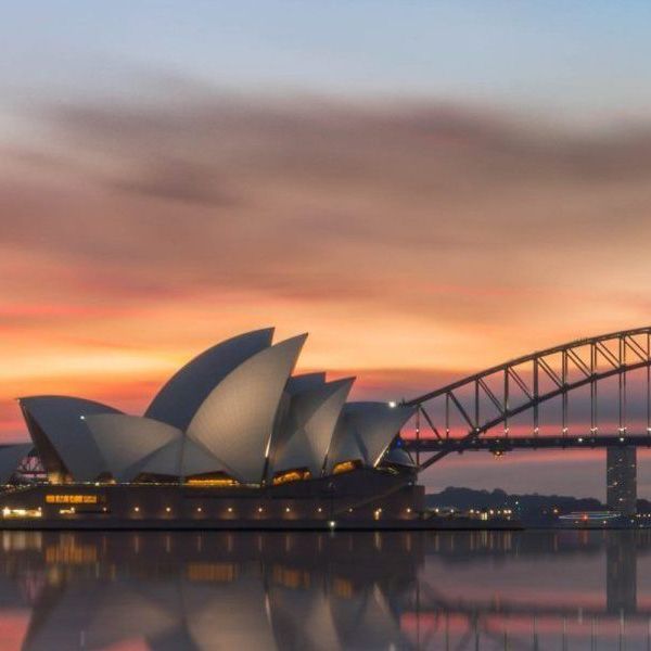 Het operagebouw in Sydney weerspiegelt zich in het water bij zonsondergang