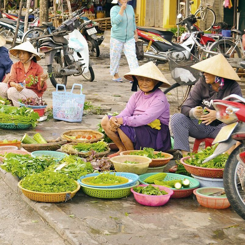 Vietnamese verkoopsters zitten op straat achter hun uitgestalde groenten