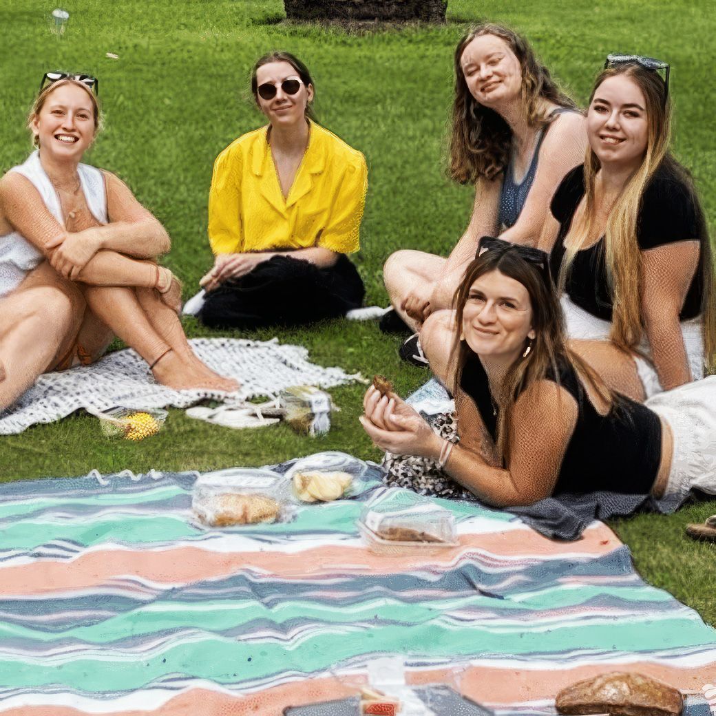 Een groep meiden zit op een deken in het gras.