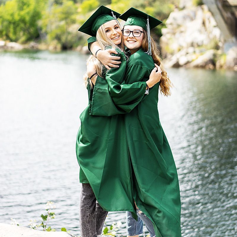 Twee vrouwelijke afgestudeerden omhelzen elkaar voor een waterpartij.