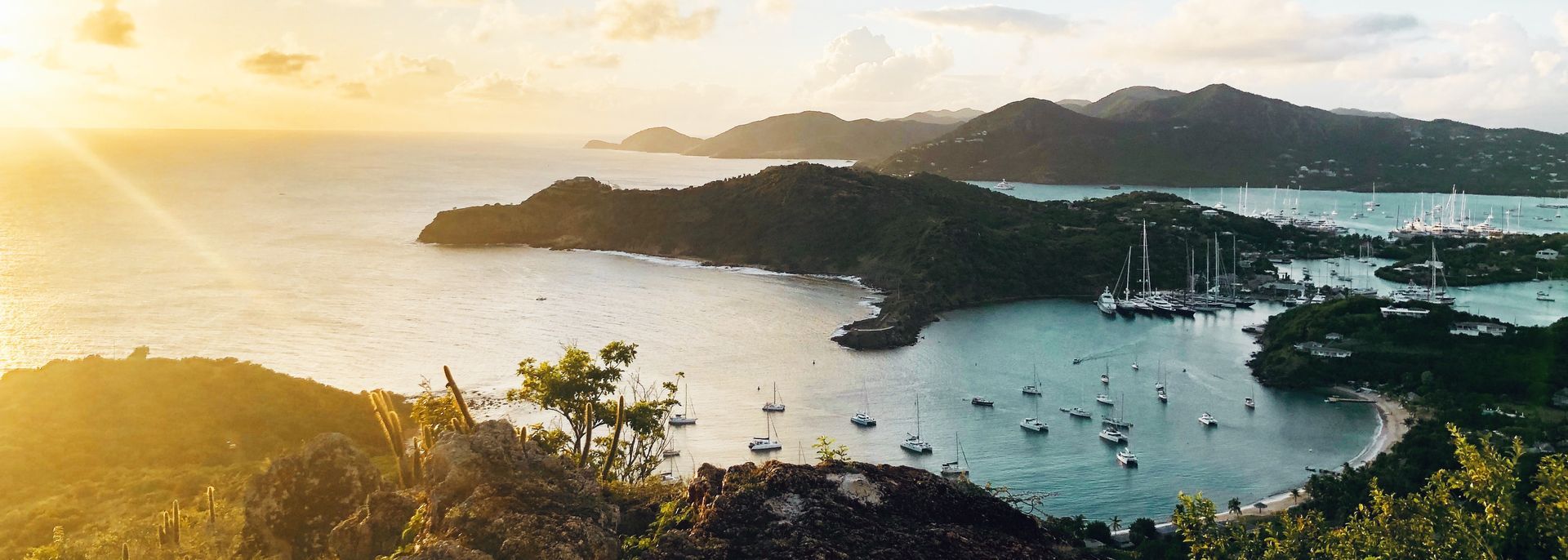 Er liggen veel boten in het water en op de achtergrond is een zonsondergang te zien.