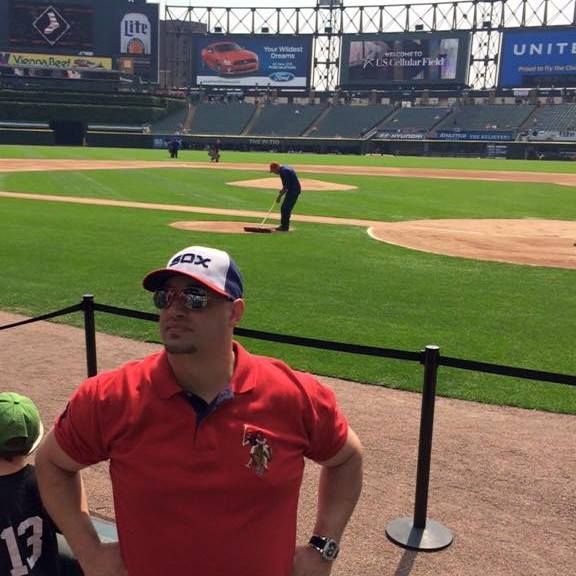A man wearing a fox hat stands in front of a baseball field