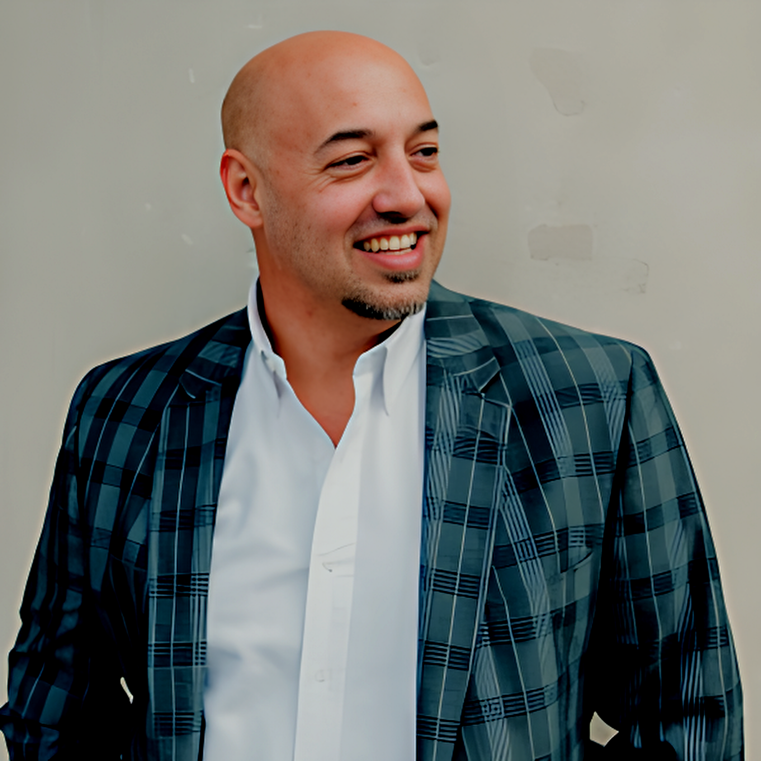 A bald man wearing a plaid jacket and white shirt smiles