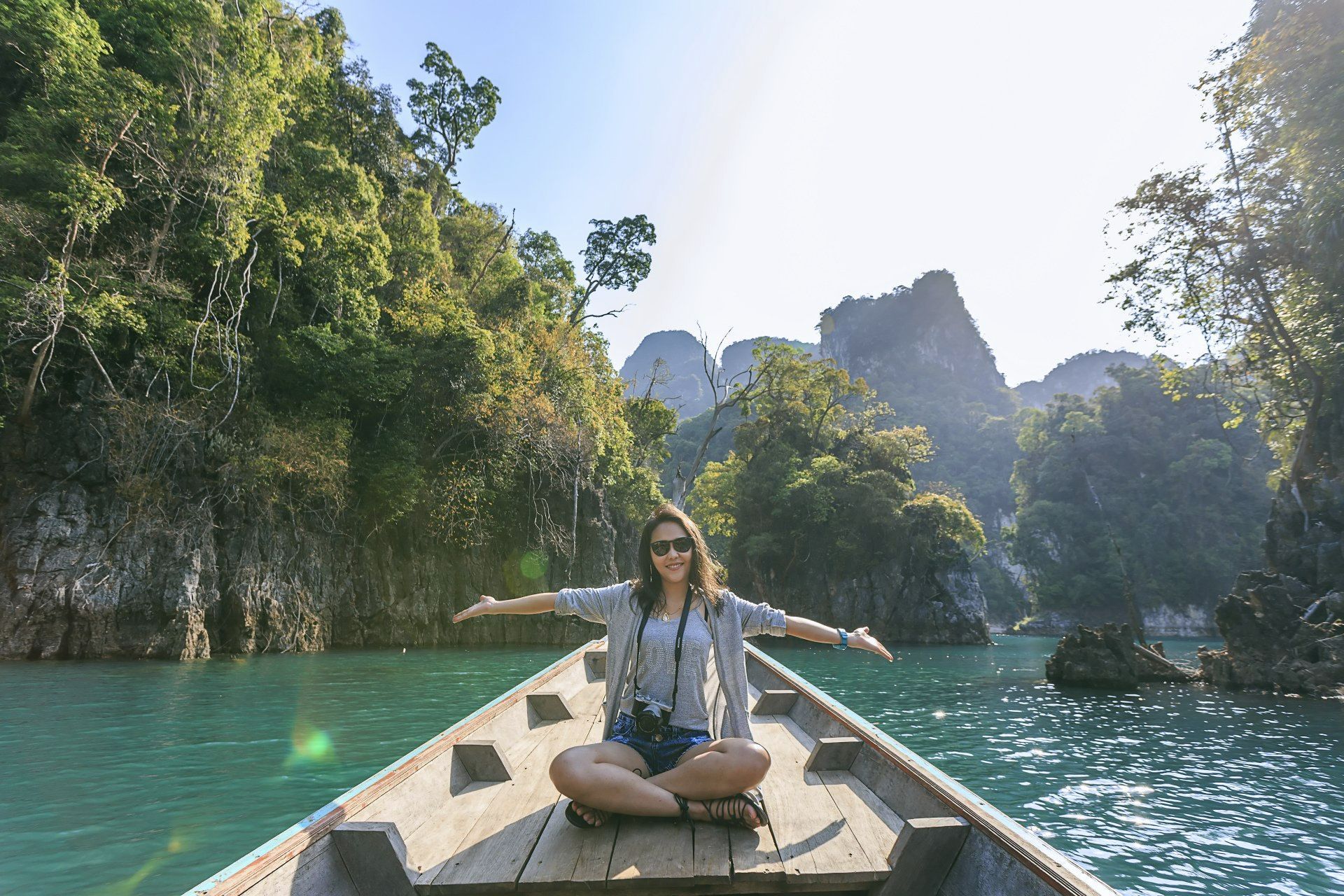A woman is sitting in a boat on a lake with her arms outstretched.