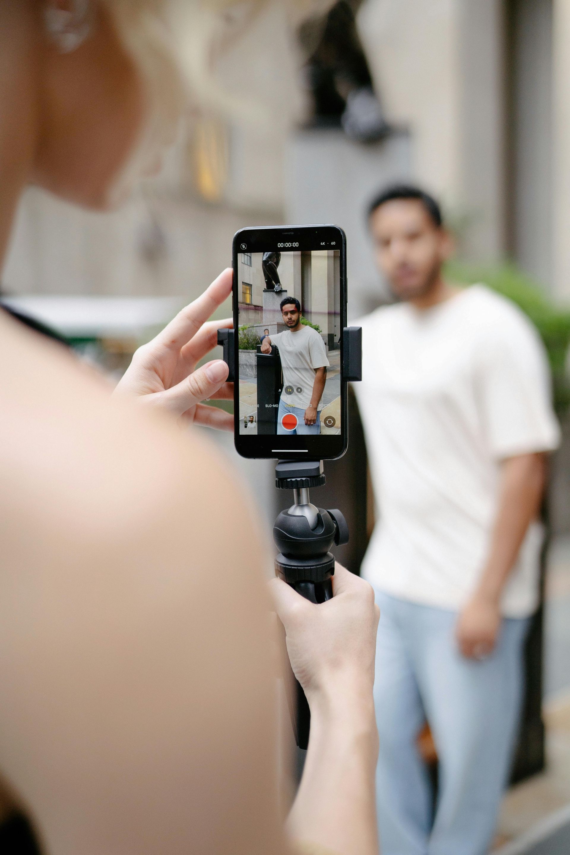 A woman is taking a picture of a man with a cell phone on a tripod.