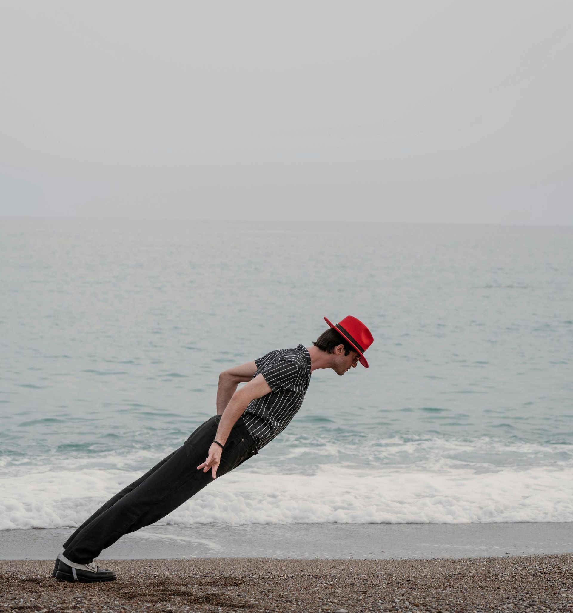 A man in a red hat is doing push ups on the beach