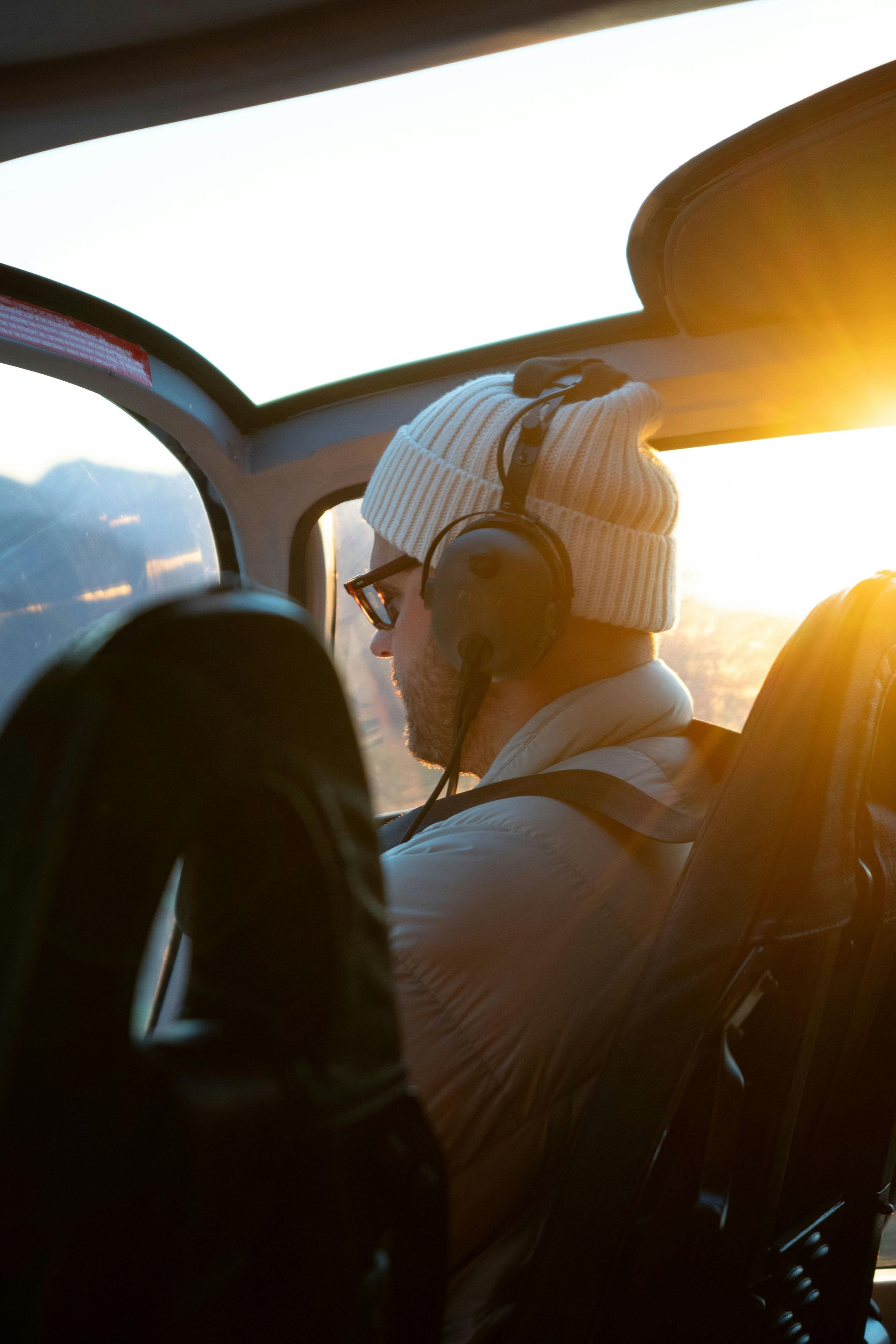 A man wearing headphones is sitting in the cockpit of a helicopter.