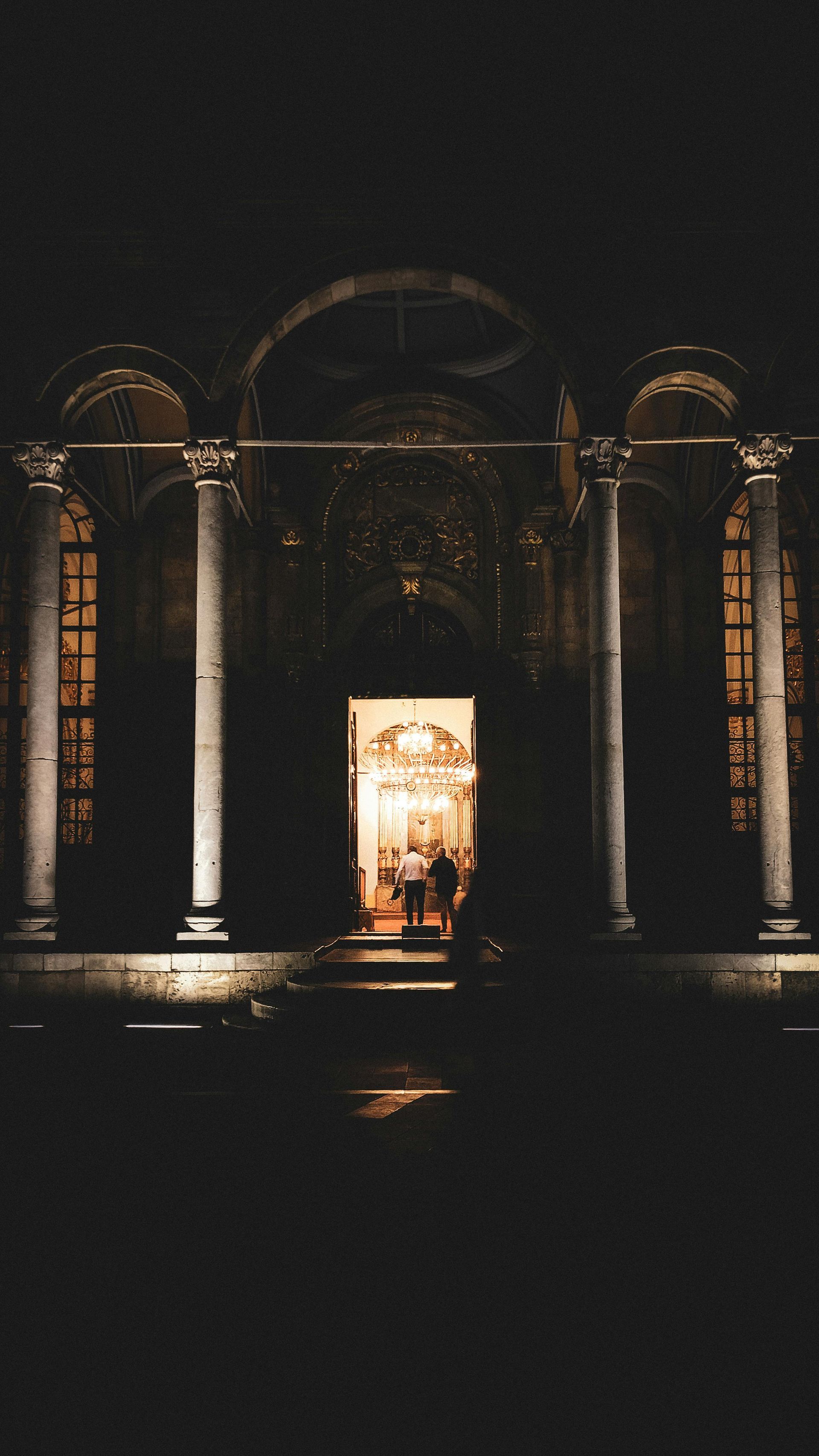 A church is lit up at night with a man standing in the doorway.