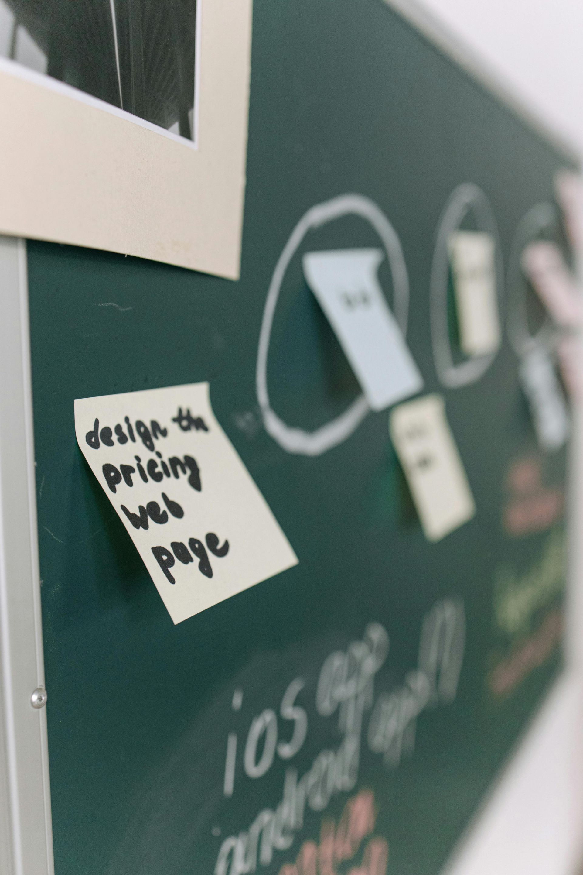 A sticky note on a blackboard that says design the pricing web page