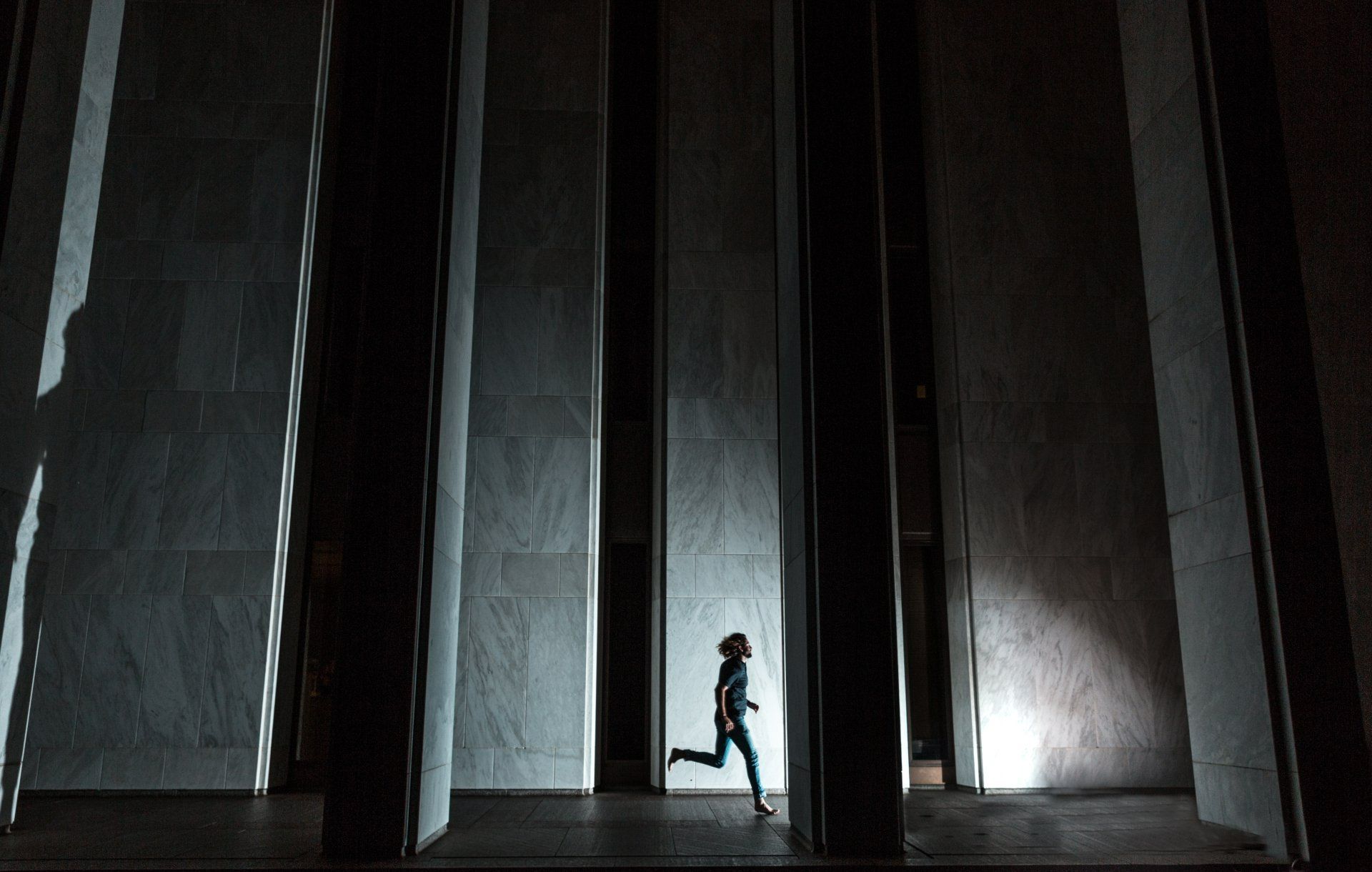 A person is running through a dark room with columns.