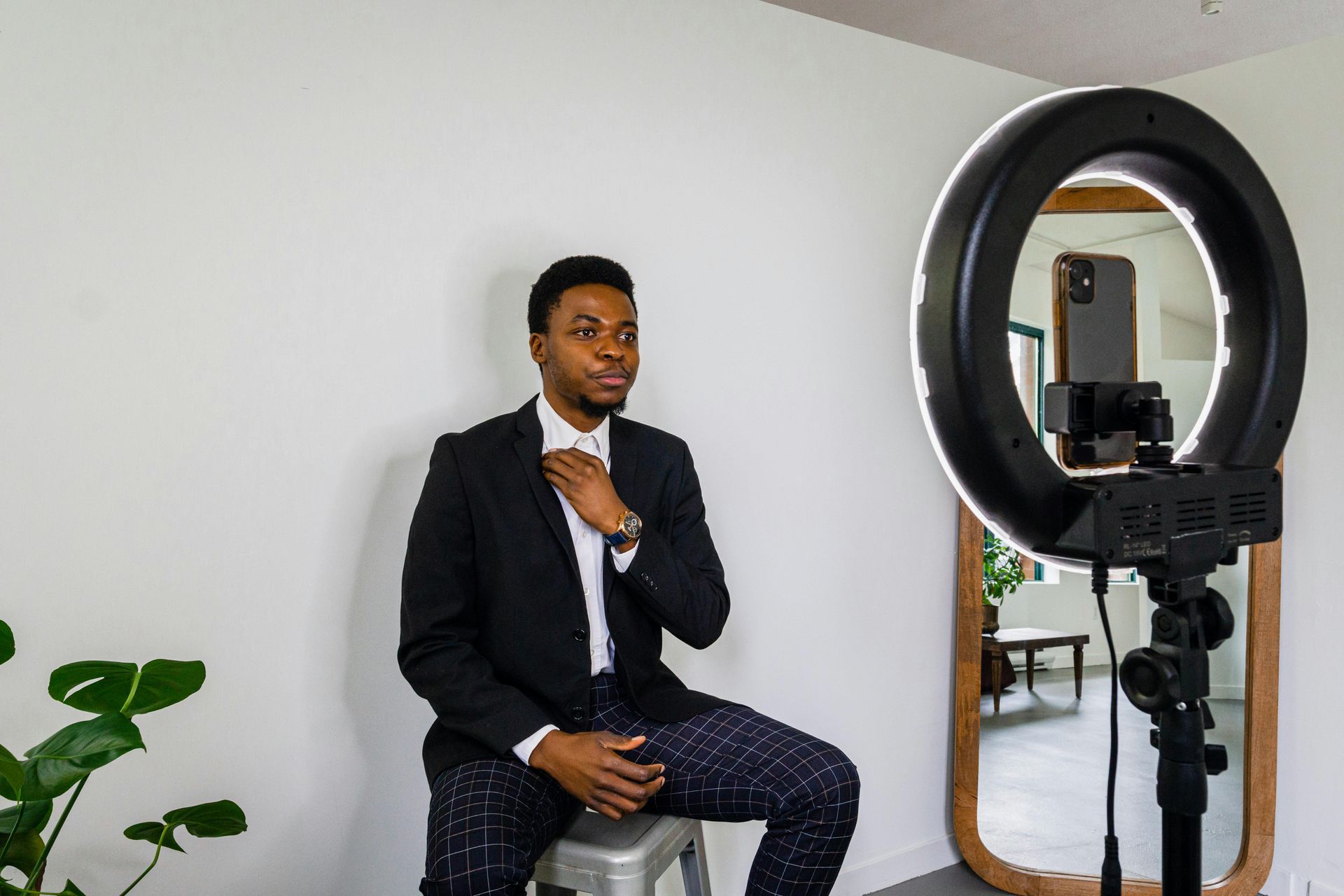 A man in a suit is sitting on a stool in front of a ring light.